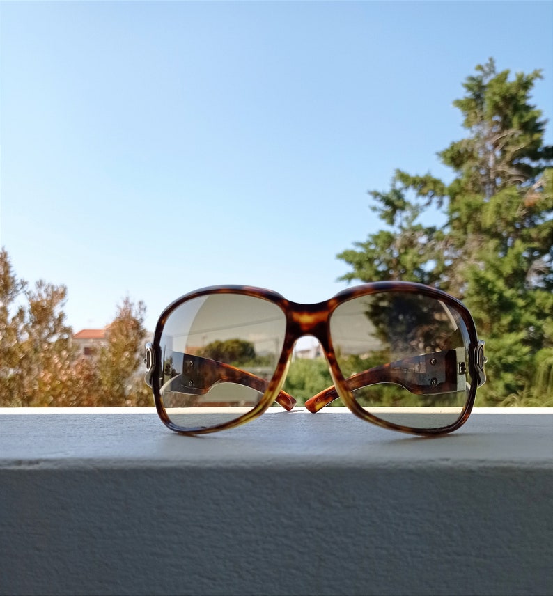 Puede incluir: Gafas de sol de carey con lentes marrones. Las gafas est&aacute;n sobre una superficie blanca.