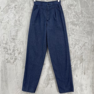 Puede incluir: Un pantalón de mezclilla azul oscuro de cintura alta con pliegues. El pantalón tiene cierre de botón y trabillas para cinturón.