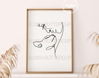 Op de afbeelding: Een zwart-witte lijntekening van een gezicht in een gouden lijst op een witte plank. De tekening is een doorlopende lijn en het gezicht kijkt omhoog. De plank staat tegen een witte muur en er zijn twee gedroogde palmbladeren aan weerszijden van de lijst.