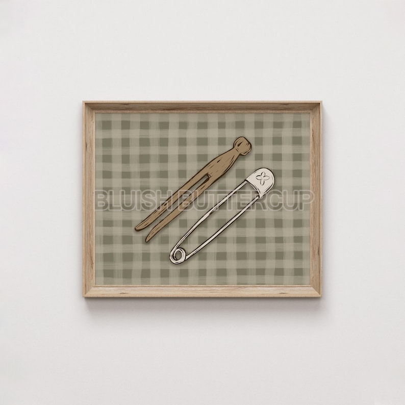 May include: A framed print with a brown and white gingham pattern background. A wooden clothespin and a safety pin are placed on the gingham pattern.