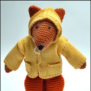 Puede incluir: Un zorro de punto que lleva un impermeable amarillo con capucha. El zorro tiene un pelaje naranja y una nariz negra.