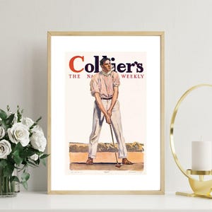 May include: Framed vintage Collier's magazine cover art showing a golfer in a light pink shirt and white trousers. The magazine title, "Collier's The National Weekly," is in red and blue. The artwork is presented in a gold frame.