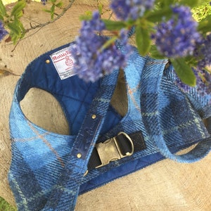 May include: A blue and brown tweed dog harness with a blue quilted lining and a brass buckle. The harness has a label that reads "Harris Tweed" and is made in Scotland.