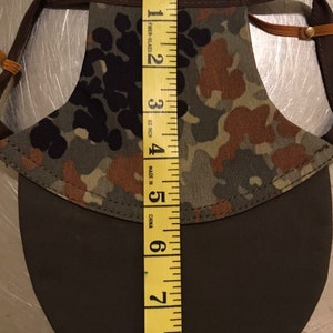 May include: A brown and green camouflage dog sun hat with a brown brim. The hat is measured with a yellow tape measure, showing a size of 6 inches.