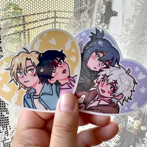 May include: Four illustrated characters on heart-shaped stickers. The characters are drawn in a cartoon style with large eyes and bright colors. The stickers are printed on a white background with a light pink and yellow design.
