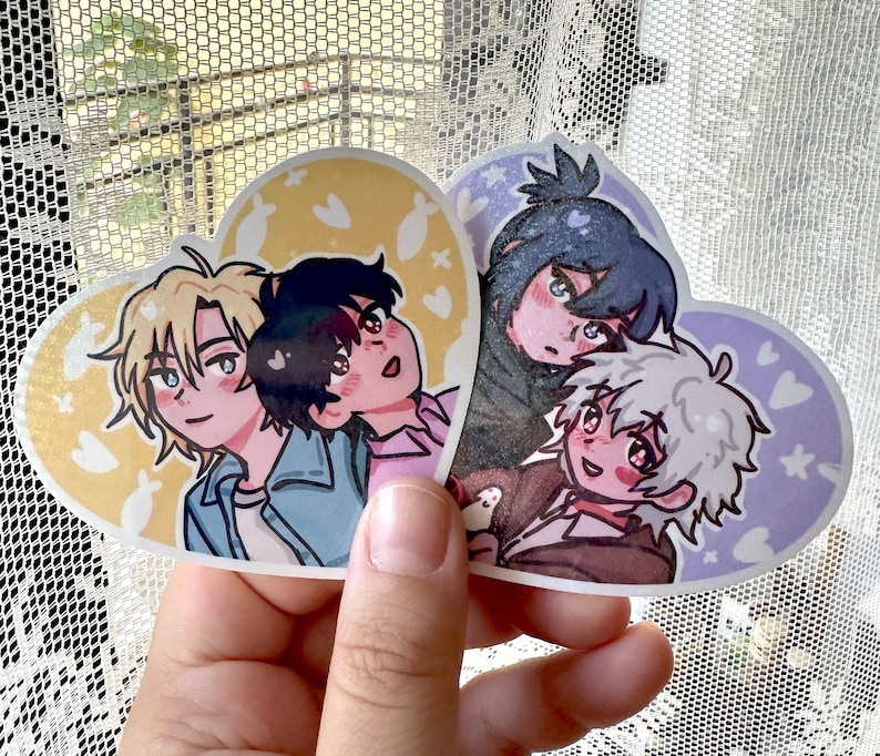 May include: Four illustrated characters on heart-shaped stickers. The characters are drawn in a cartoon style with large eyes and bright colors. The stickers are printed on a white background with a light pink and yellow design.