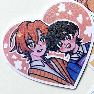 May include: A heart-shaped sticker with two anime characters. The character on the left has orange hair and is wearing a striped sweater. The character on the right has black hair and is wearing a blue and white striped shirt. The background is pink with white flowers and hearts.