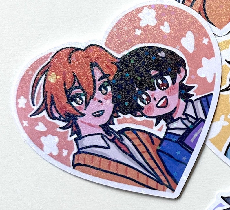 May include: A heart-shaped sticker with two anime characters. The character on the left has orange hair and is wearing a striped sweater. The character on the right has black hair and is wearing a blue and white striped shirt. The background is pink with white flowers and hearts.