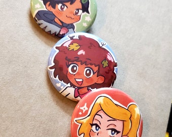 May include: Three round button pins featuring cartoon characters. The top pin features a boy with dark hair and a green shirt. The middle pin features a girl with brown hair and a white shirt. The bottom pin features a girl with blonde hair and a black shirt.