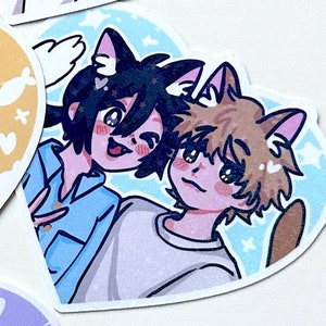 May include: A heart-shaped sticker with two cartoon characters with cat ears. The character on the left has blue hair and is wearing a light blue shirt. The character on the right has brown hair and is wearing a light purple shirt. The background is a light blue with white stars.