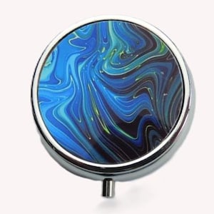 May include: Round pill box with a silver metal rim and a blue, green, and black marbled design.