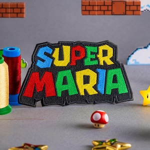 Może przedstawiać: Kolekcja przedmiotów z motywem Super Mario, w tym naszywka z napisem "Super Maria", złota szpulka nici, grzyb, gwiazda i złote monety. Tło przedstawia pikselowe chmury i ceglane bloki.