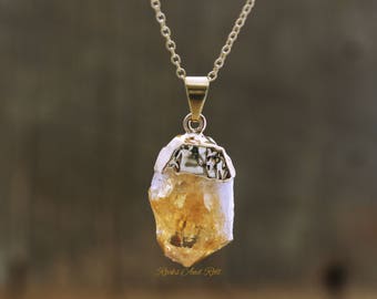 Puede incluir: Un collar de cadena de oro con un colgante hecho de un cristal de citrino crudo, claro y amarillo. El cristal está engastado en un bisel de oro.