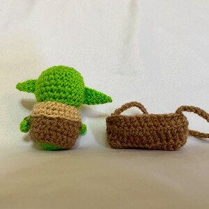 Puede incluir: Una mu&ntilde;eca Yoda de crochet verde y marr&oacute;n con una bolsa de crochet marr&oacute;n.