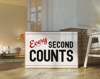 May include: A white framed motivational poster with a red and black graphic that reads "Every Second Counts". The poster is leaning against a wooden cabinet in a room with a white couch and a wooden floor.