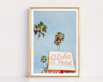 Könnte beinhalten: Ein Schild im Vintage-Stil mit dem Text "Aloha Hotel" in rosa Schrift auf rotem und orangefarbenem Hintergrund. Das Schild steht vor einem blauen Himmel mit Palmen.