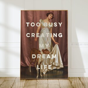 Peut inclure: Une affiche de style vintage avec une femme en robe blanche et un chien. Le texte sur l'affiche dit "Too Busy Creating My Dream Life".