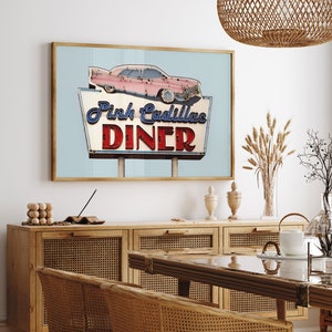 May include: A framed print featuring a vintage sign for the "Pink Cadillac Diner." The sign has a light blue background with a pink car and the diner's name in blue and red lettering. The print is displayed in a room with wooden furniture.