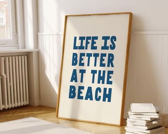 May include: A framed print with the text "LIFE IS BETTER AT THE BEACH" in blue letters on a white background. The frame is made of wood and has a light brown finish.