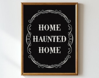 May include: A framed black and gold sign with the words "HOME HAUNTED HOME" in white, centered on the black background. The text is surrounded by a decorative white border. The frame is a gold color.