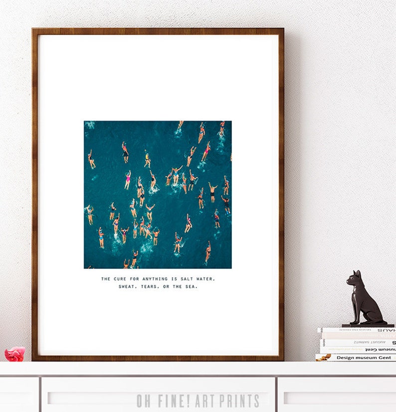 May include: A framed print with a photograph of a group of people swimming in the ocean. The text below the image reads "The cure for anything is salt water, sweat, tears, or the sea."