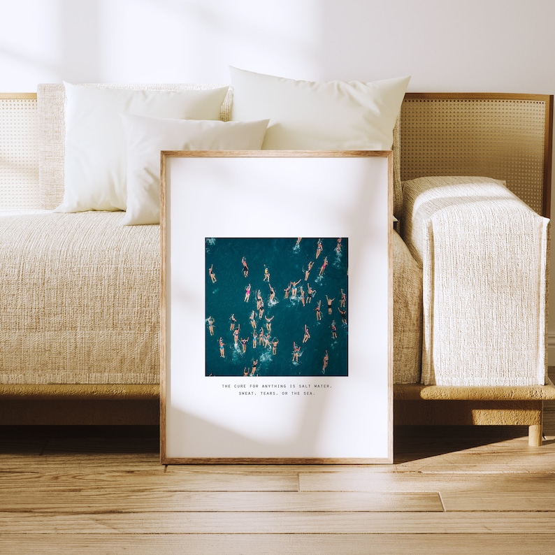 May include: A framed print with a photograph of a group of people swimming in a turquoise ocean. The text "The cure for anything is salt water. Sweat, tears, or the sea." is printed below the image.