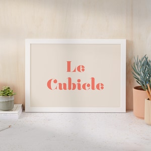 May include: A white framed print with a beige background and the text "Le Cubicle" in pink.