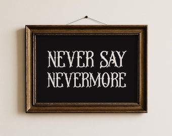 May include: A framed black print with the words "NEVER SAY NEVERMORE" in white, ornate lettering. The frame is a dark, ornate gold color, and the print is hanging against a white wall.