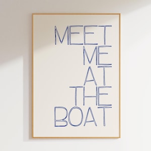 May include: A framed art print with the words "MEET ME AT THE BOAT" in blue handwritten style on an off-white background. The frame is a light brown color. The artwork is displayed on a white wall.