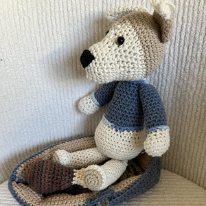 May include: A crocheted dog toy in a blue and brown basket. The dog is white with brown ears and a blue shirt. The basket has a brown and beige striped pattern.