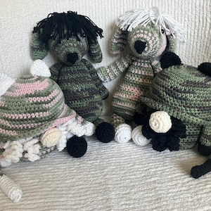 May include: Four handmade crochet dolls and hats. The dolls are in the shape of dogs, with black or white yarn hair, and are primarily green, pink, and black. The hats are in the shape of gnomes, with white and black accents.