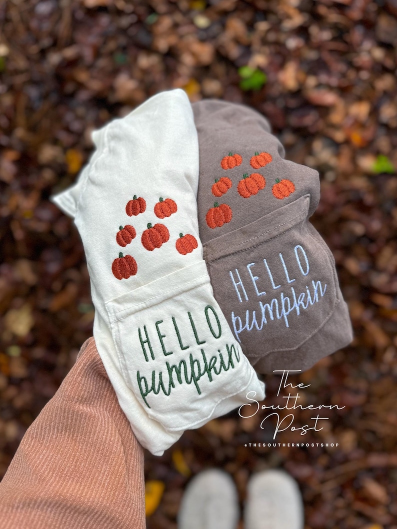 May include: Two white and brown t-shirts with embroidered pumpkins and the text "Hello Pumpkin". The shirts are folded and held in a person's hand. The text "The Southern Post" is visible at the bottom of the image.