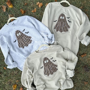 May include: Three sweatshirts with a plaid ghost design and bats. The sweatshirts are in grey, beige, and white.
