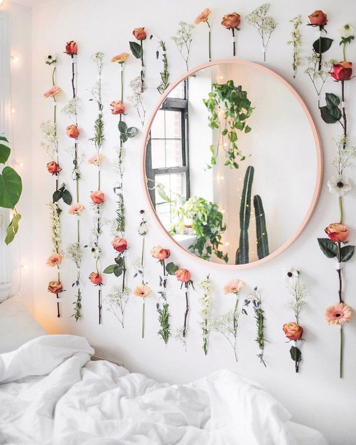 Pink, red and white flowers attached to the wall around a round mirror