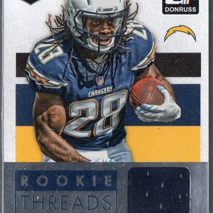 May include: A football trading card featuring Melvin Gordon, a rookie player for the Los Angeles Chargers. The card is a Donruss Rookie Threads card and features a close-up of Gordon in his uniform with a football in his hand. The card has a silver background with a blue and yellow jersey patch.