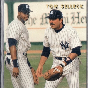 May include: Baseball card showing two baseball players in pinstripe uniforms and caps. The card has the text "TOM SELLECK" at the top and "Mr. Baseball" at the bottom. The players are wearing gloves and appear to be on a baseball field.