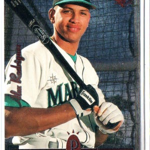 Puede incluir: Tarjeta de béisbol con Alex Rodríguez con el uniforme de los Marineros de Seattle. Sostiene un bate Louisville Slugger y lleva una gorra de los Marineros. La tarjeta tiene el texto "Premier Prospects".