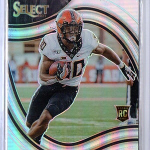 May include: A football trading card featuring a player in a white jersey with a black and orange helmet. The card has a holographic background with a black and gold border. The player's name is "Chuba Hubbard" and the team is "Cowboys".