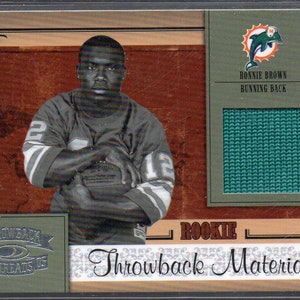 May include: A football card featuring a black and white photo of a football player wearing a green jersey with the number 12 on it. The card has a green and white background with the text "Rookie Throwback Materials" and "Ronnie Brown Running Back".