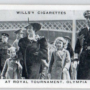 Puede incluir: Imagen en blanco y negro de una tarjeta de cigarrillos vintage que muestra a una familia real en el Torneo Real en Olympia. La tarjeta muestra a un grupo de personas, incluidos militares y civiles, caminando al aire libre. El texto "WILLS'S CIGARETTES" está en la parte superior.