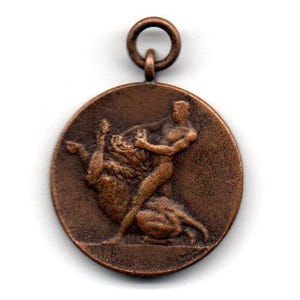 May include: A bronze medal with a depiction of a person wrestling a bull. The medal has a loop at the top for hanging.