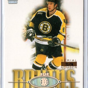 Op de afbeelding: Een hockey trading card met Joe Thornton van de Boston Bruins. De kaart toont Thornton in zijn zwart-gouden Bruins-shirt, met een hockeystick. De kaart heeft de tekst "Bruins" en "Joe Thornton". Serienummer 71/74.