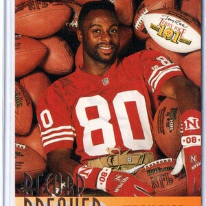 Pode incluir: Um cartão colecionável Topps Stadium Club apresentando Jerry Rice em uma camisa vermelha com o número 80, usando luvas vermelhas e brancas, cercado por bolas de futebol. O cartão inclui o texto Record Breaker e Jerry Rice na base.