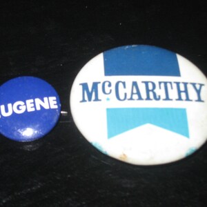 May include: Two blue and white political campaign buttons. The larger button says "McCarthy" in blue letters on a white background with a blue and white ribbon. The smaller button says "Eugene" in white letters on a blue background.