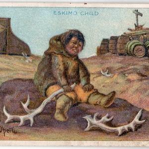 May include: A young Eskimo child wearing a brown fur coat sits on a rock holding two white antlers. The child is looking down at the antlers. The background shows a wooden structure and a snowy landscape.