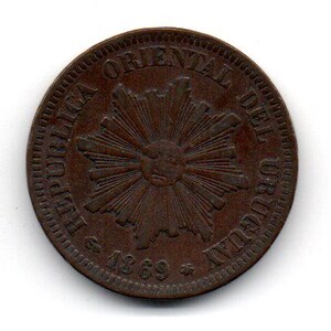 May include: A copper-colored coin with the text "REPUBLICA ORIENTAL DEL URUGUAY" and "$ 1869 $" around a stylized sunburst design.