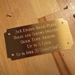 May include: A rectangular brass plate with rounded corners and etched text. The text reads "2x4 ETCHED BRASS PLATE HOLES AND SCREWS INCLUDED QUICK TURN AROUND UP TO 5 LINES UP TO APRX. 25 CHARACTERS/LINE." Several screws are scattered around the plate.