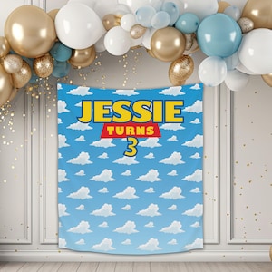 May include: A blue and white backdrop with a red and yellow banner that says "Jessie Turns 3". The backdrop is decorated with white clouds on a blue background.
