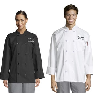 May include: Two white chef coats with black buttons and a black pocket on the left side. The left coat is black and the right coat is white. Both coats have embroidered names and titles on the right side of the chest. The left coat says "Paige Spencer, Executive Chef" and the right coat says "Mark Spencer, Private Chef".