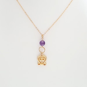May include: A gold chain necklace with a purple amethyst bead and a gold pendant featuring a stylized heart with a cross inside.